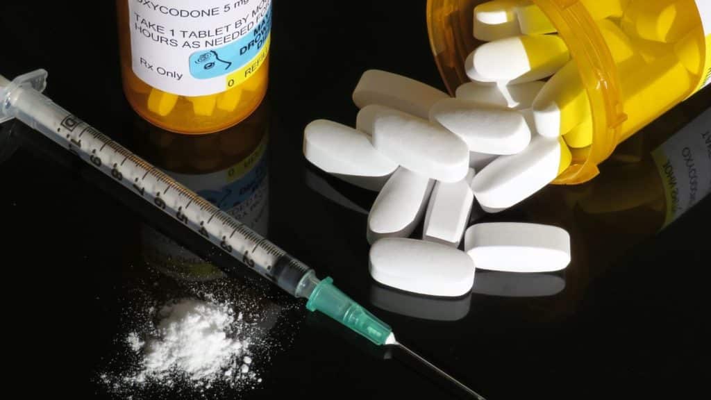 Pill bottle with heroin needle and cocaine on table